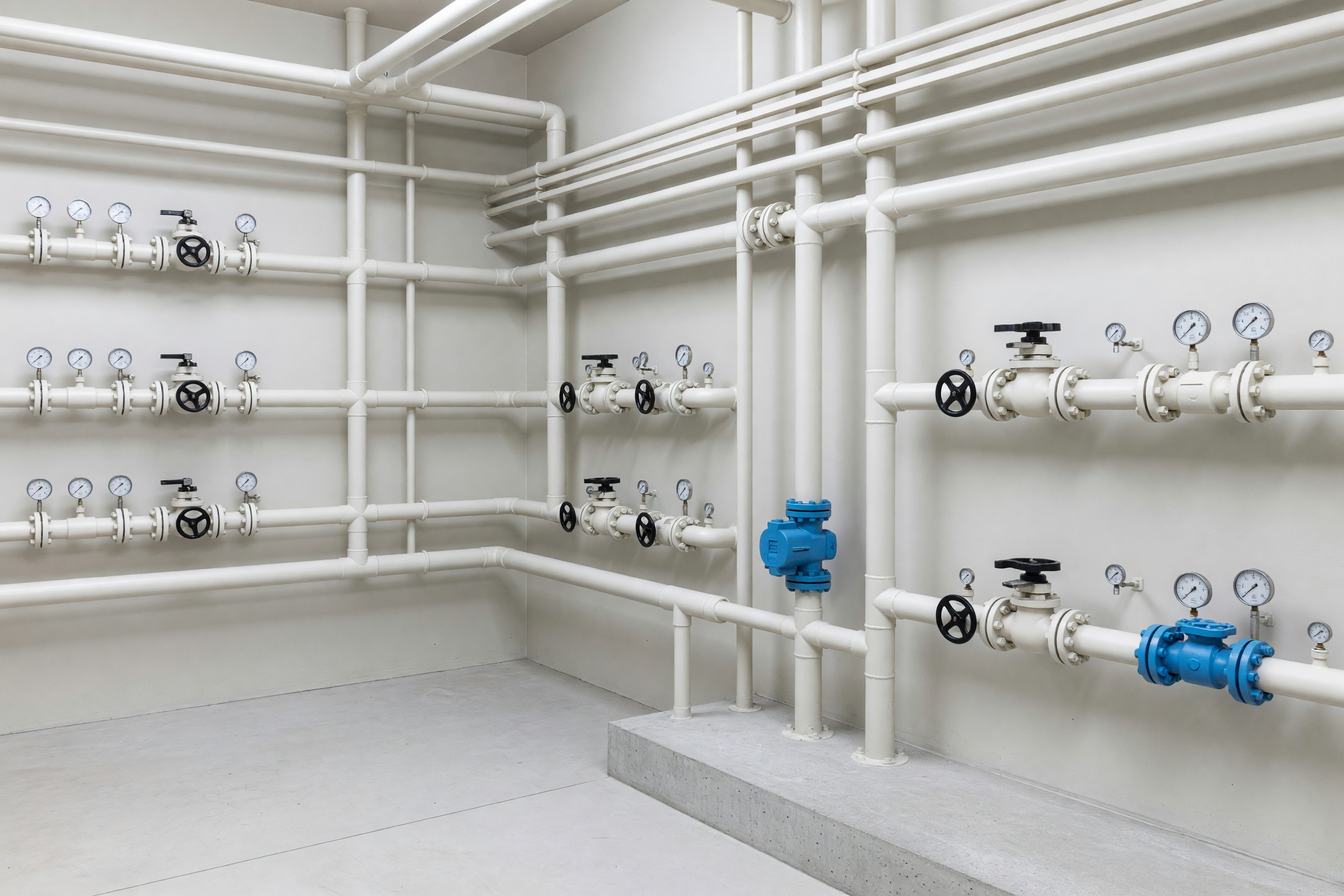 Unpeopled commercial plant room with pale pipework, valves and a low concrete plinth