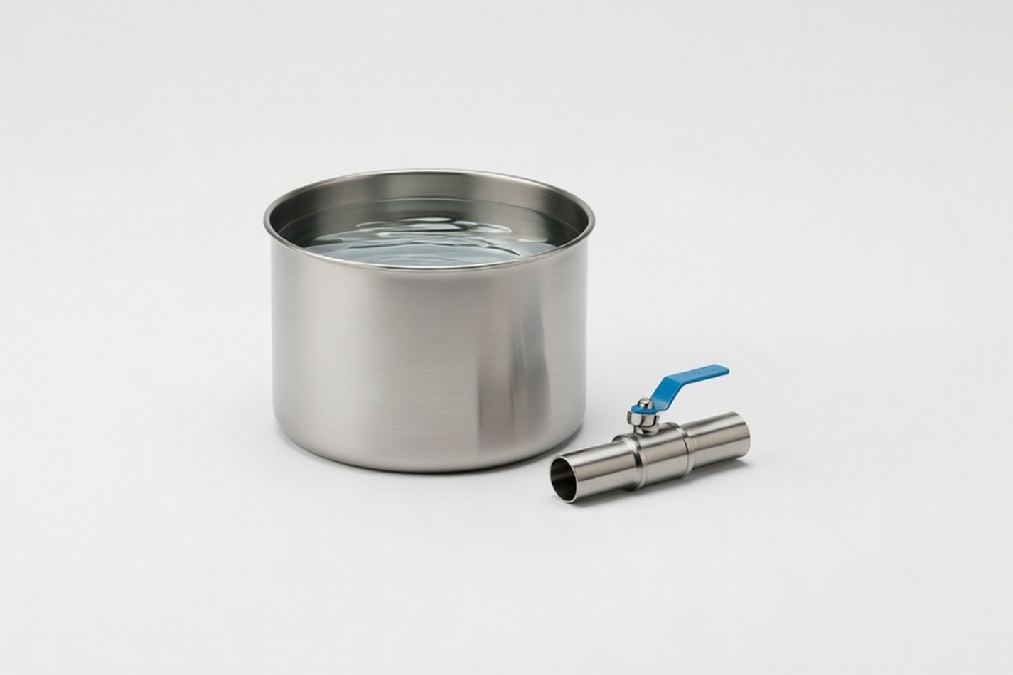 Clear water pouring into a stainless steel vessel beside a length of pipework