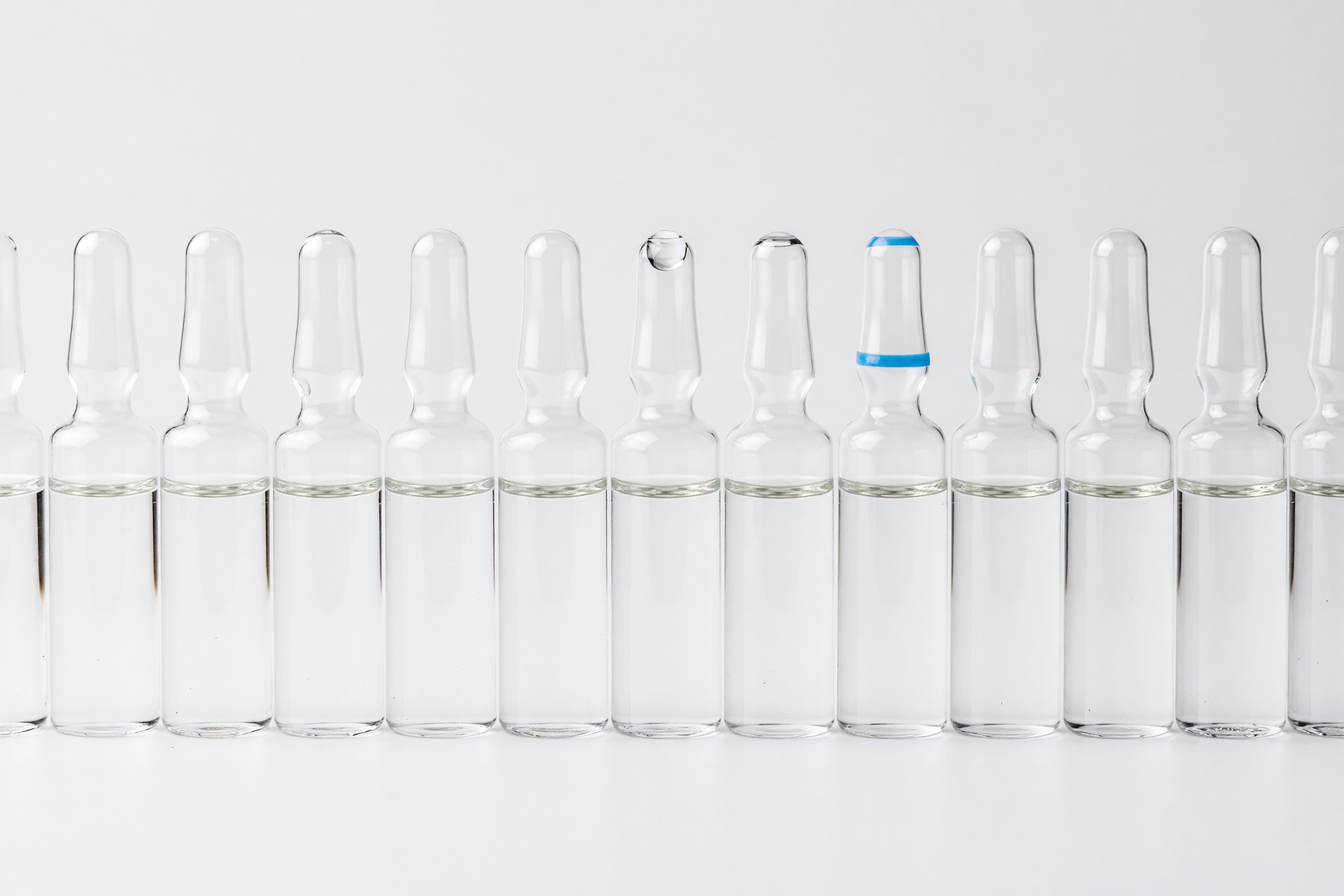 A row of clear glass pharmaceutical ampoules filled with a clear sterile liquid, on a clean studio ground