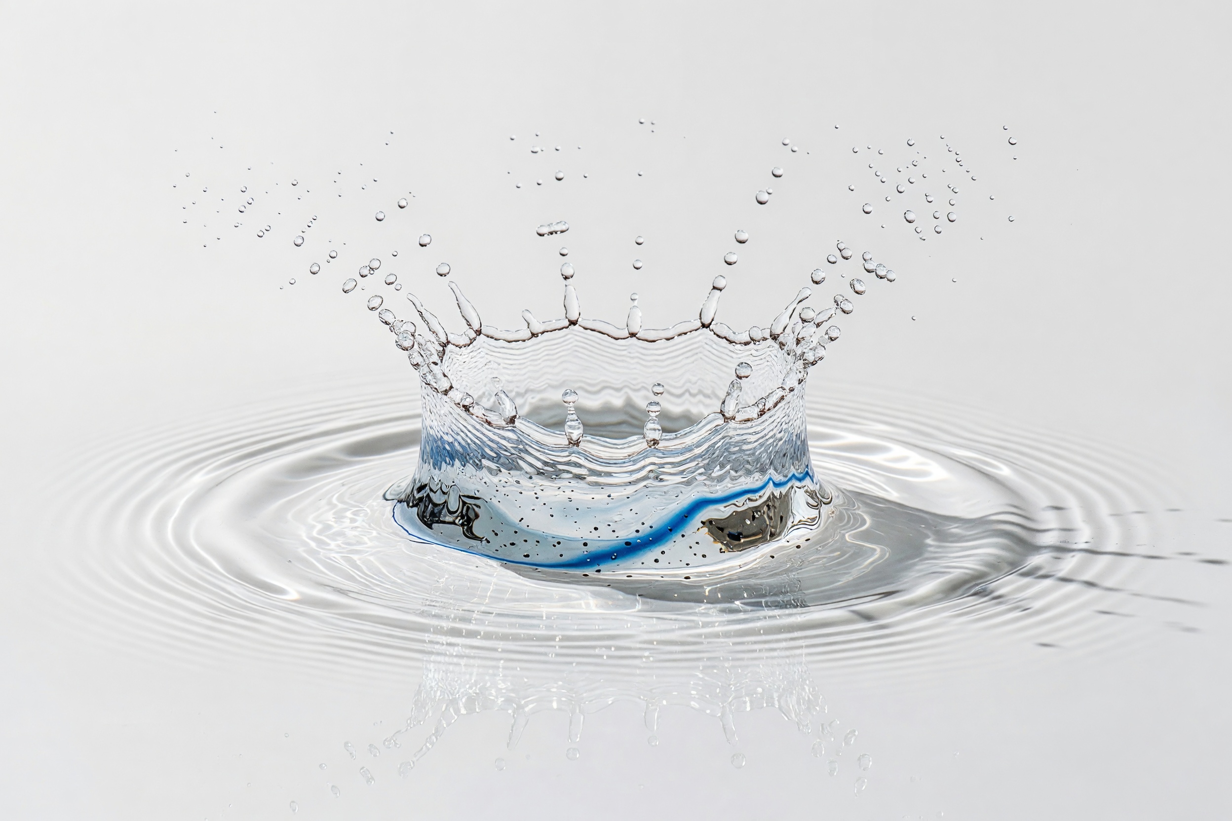 A crisp splash crown of clear water with fine droplets and ripples, on a clean studio ground